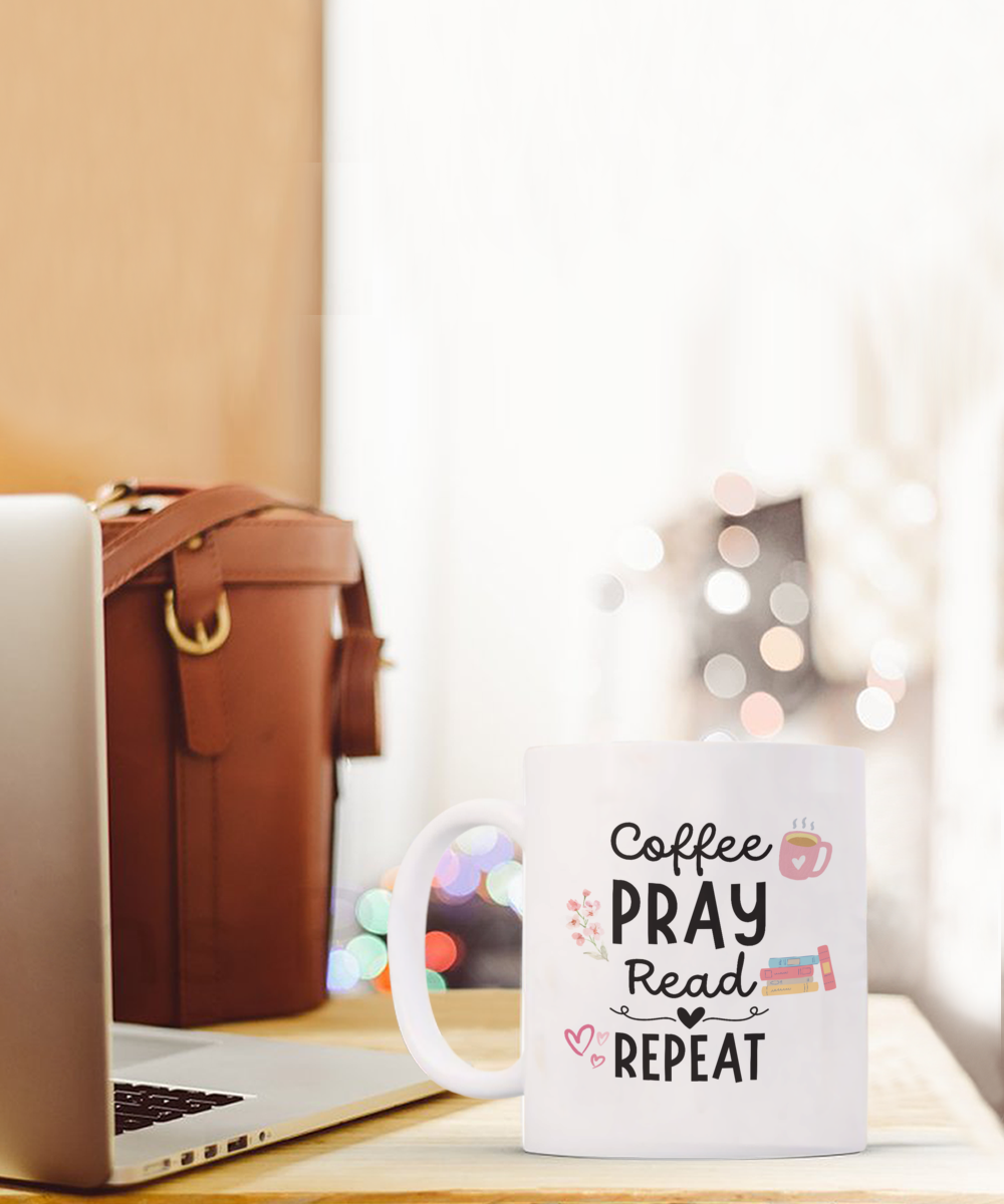 A Coffee Pray Read Repeat mug, perfect for readers, sits by a laptop and brown bag. This exclusive item is uniquely printed and shipped from the USA, available only for a limited time.