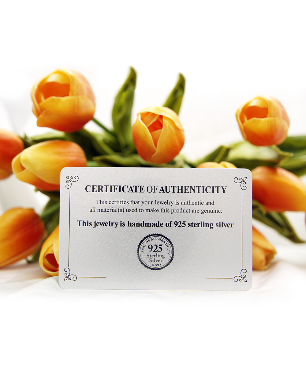 A certificate of authenticity for a To Grandma, Strong Lady - Cross Dancing Necklace by Gearbubble placed in front of a bouquet of orange tulips.