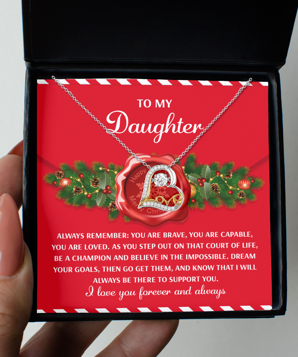 A box showcases the Daughter-Be A Champion - Love Dancing Necklace with a message card, "To my daughter... I love you forever and always," set against a festive red background with pine leaves, capturing the essence of everlasting love.