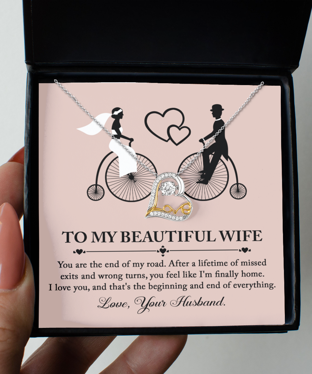 A beautiful To Wife, I'm Finally Home - Love Dancing Necklace in a box adorned with an illustration of a bride and groom on bicycles. The box, featuring the message "To My Beautiful Wife," expresses love and appreciation from "Your Husband." This necklace is crafted with .925 Sterling Silver, making it a timeless keepsake.