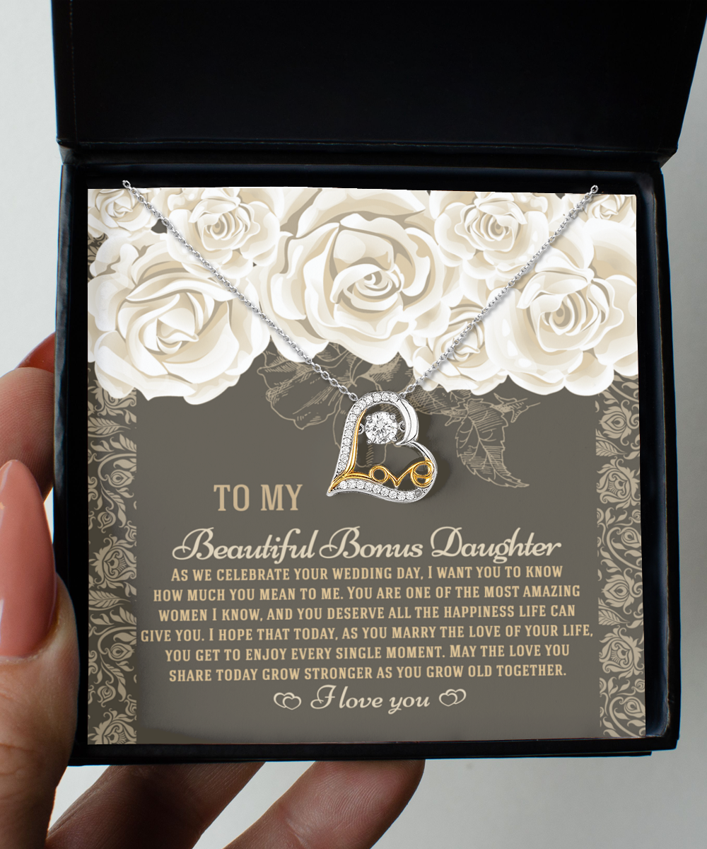 The "To Bonus Daughter - Grow Old Together - Love Dancing Necklace" is a heart-shaped pendant crafted from .925 Sterling Silver, beautifully presented in a box alongside a card. The card features an emotional message to a daughter on her wedding day, adorned with floral illustrations.