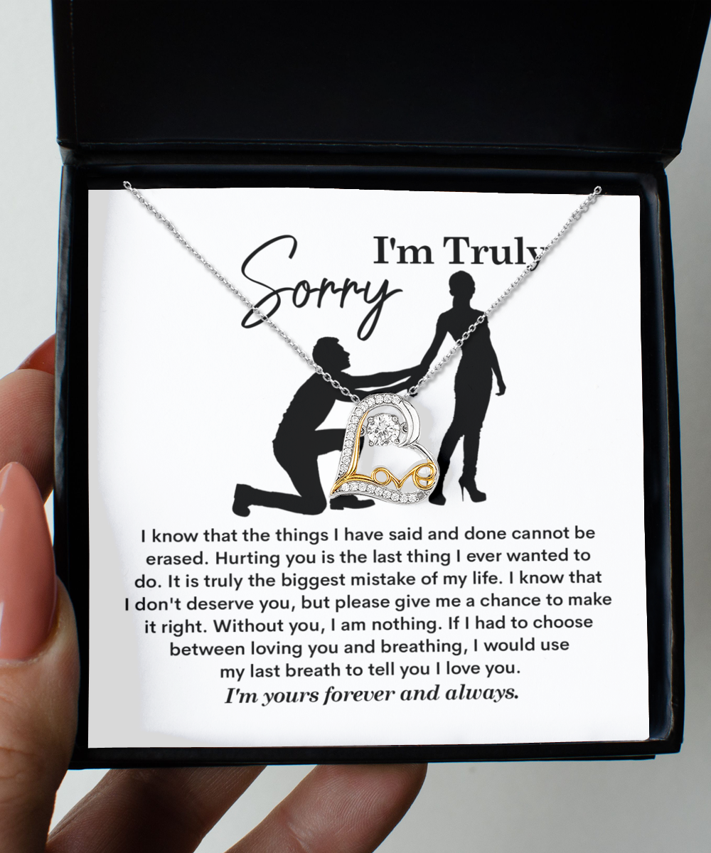 A Sorry-My Last Breath - Love Dancing Necklace, featuring a heart-shaped pendant crafted from .925 Sterling Silver, is placed on top of a note with the heading "I'm Truly Sorry" and an illustration of a person on one knee offering their hand to another person.