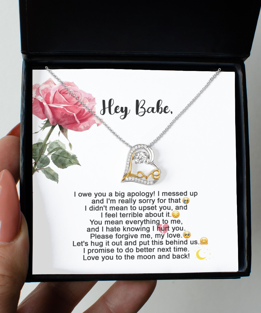 A "Sorry-Hug It Out - Love Dancing Necklace," featuring a heart-shaped pendant on a 14k gold chain, is displayed against a card adorned with an apology message and a pink rose illustration. The message expresses regret, love, and a promise to improve.