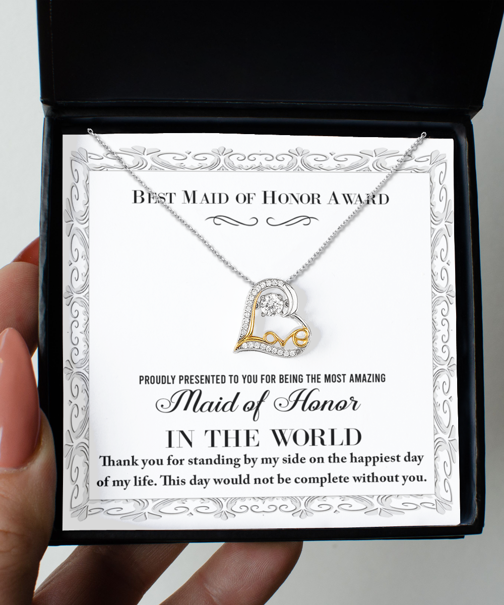 A close-up of a person's hand holding an open black jewelry box containing To Maid of Honor-Of My Life - Love Dancing Necklace. The .925 Sterling Silver necklace features a heart-shaped pendant with a small diamond. Inside the box, there's a card that reads: "Best Maid of Honor Award," adorned with an ornate border and additional text of appreciation.