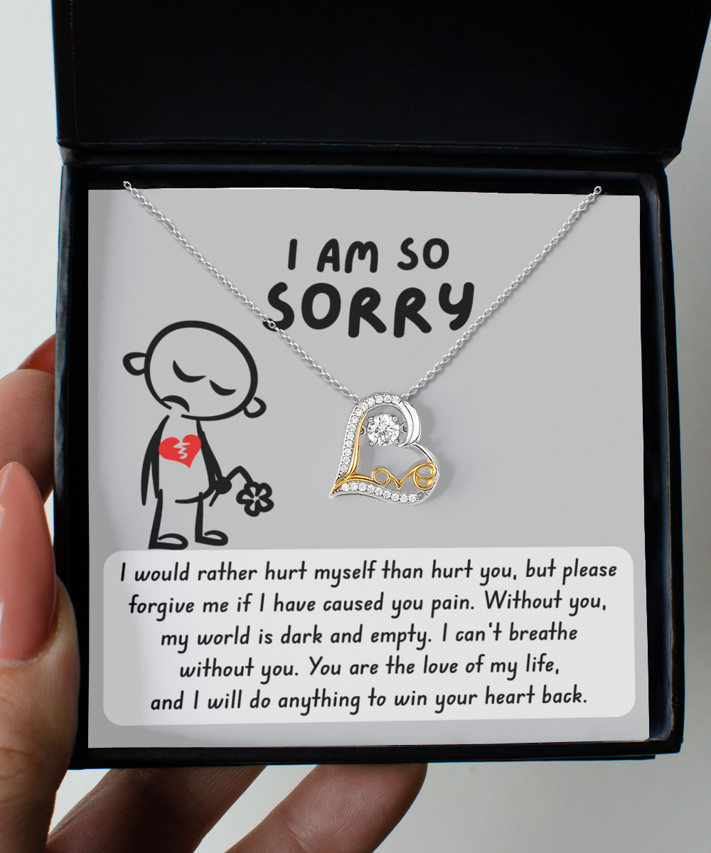 A hand holds an open jewelry box containing the Sorry-Dark And Empty - Love Dancing Necklace, a heart-shaped pendant crafted from sterling silver, accompanied by a note that reads, "I am so sorry," along with an apology and a promise to win the recipient's heart back.