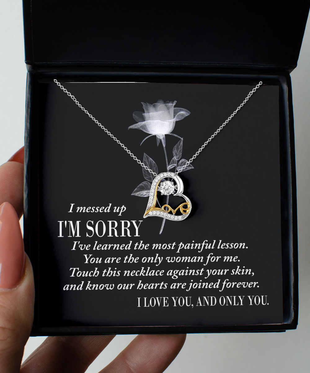 Sorry-Painful Lesson - Love Dancing Necklace: A silver, heart-shaped necklace adorned with a gold accent and a diamond, presented in a black box. The box liner features an apology message and a statement of love. Expertly crafted with genuine .925 sterling silver, it showcases the enduring beauty of AAAAA Cubic Zirconia.