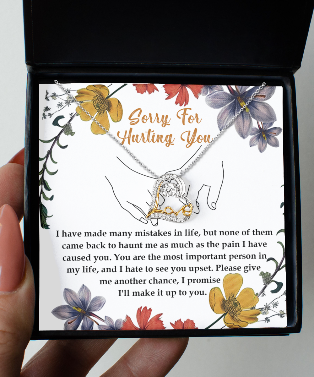 A stunning Sorry-Haunt Me - Love Dancing Necklace featuring an intertwined heart pendant, crafted in sterling silver, rests on a card that reads, "Sorry for hurting you," along with an apology message below. The card is beautifully decorated with floral illustrations.