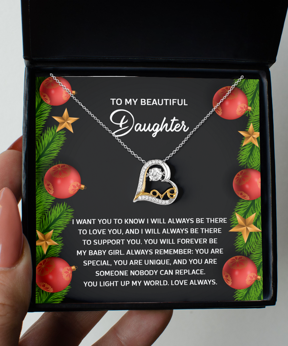 A person holds a "Daughter-Nobody Can Replace - Love Dancing Necklace" with a heart pendant in a gift box. The lid features a message of maternal love and support for a daughter, surrounded by festive decorations, making it an ideal gift for special occasions.