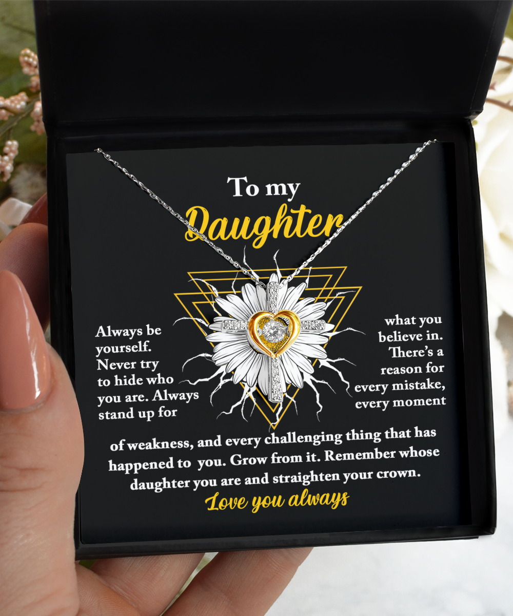 A hand holds an open black gift box displaying a stunning 14k gold Cross Dancing Necklace. The box lid reads "To my Daughter" with motivational text encouraging self-love and resilience. The message ends with "Love you always.