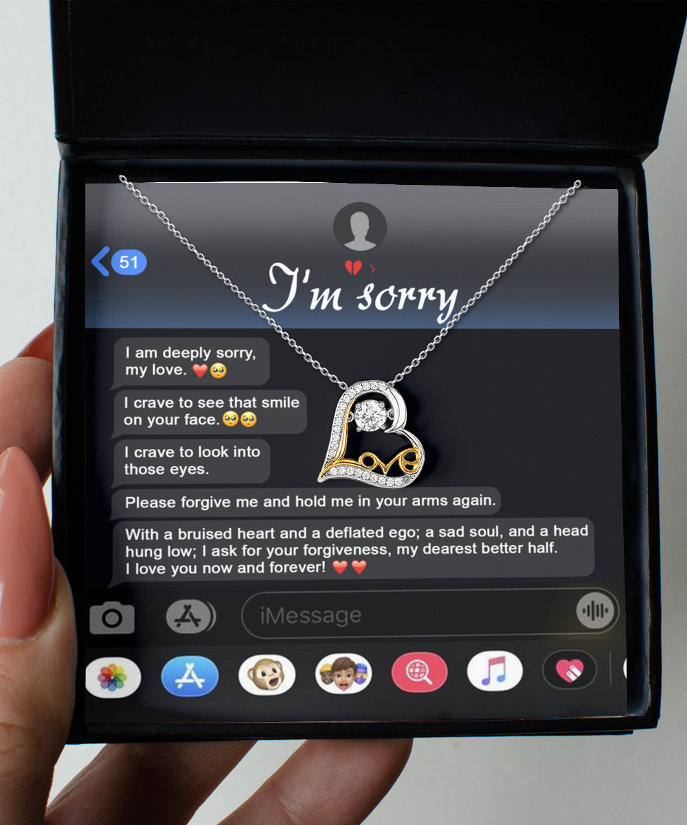 A Sorry-Rebuild Our Connection - Love Dancing Necklace, featuring a heart-shaped pendant crafted from silver and 14k gold, is placed inside a jewelry box. The background displays a message on a phone screen saying "I'm sorry" and a heartfelt apology.