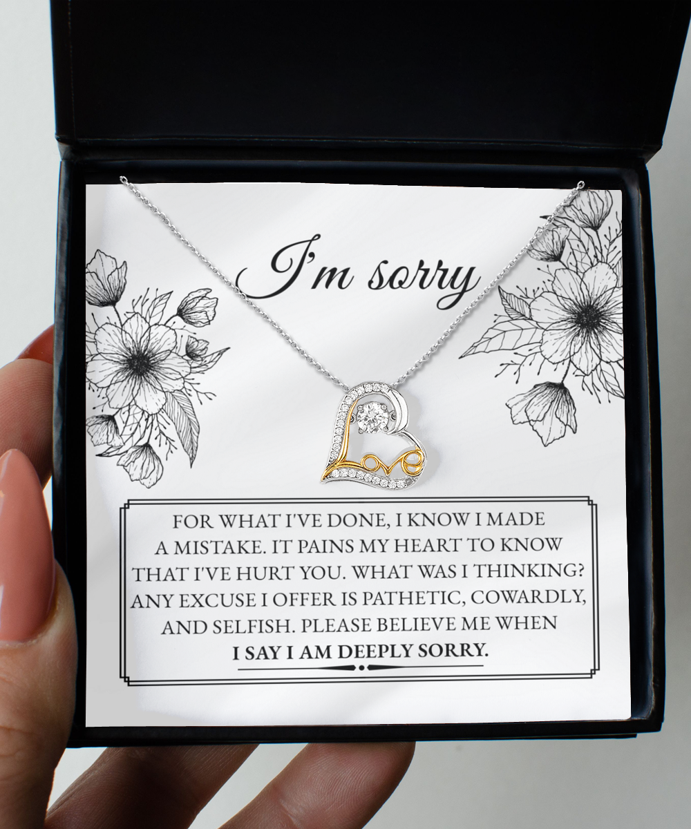 A 14k gold necklace with an intertwined heart design from the "Sorry-Made A Mistake - Love Dancing Necklace" collection is presented in a box. The text inside conveys an apology for causing pain, expressed with deep regret and a heartfelt plea to believe in the sincerity of the apology.