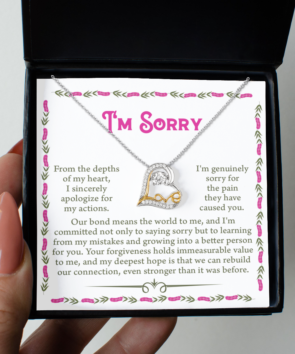 A hand holds an open box displaying the "Sorry-A Better Person - Love Dancing Necklace," a heart-shaped pendant in sterling silver, along with a handwritten apology note that reads "I'm Sorry," expressing deep regret for the harm caused.