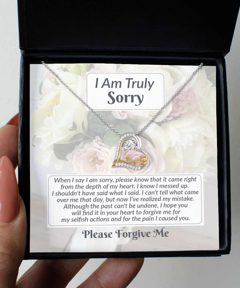 A hand holds an open jewelry box displaying the "Sorry-What I Said - Love Dancing Necklace," a heart-shaped pendant crafted in sterling silver with a note that says, "I Am Truly Sorry" and an apology message.