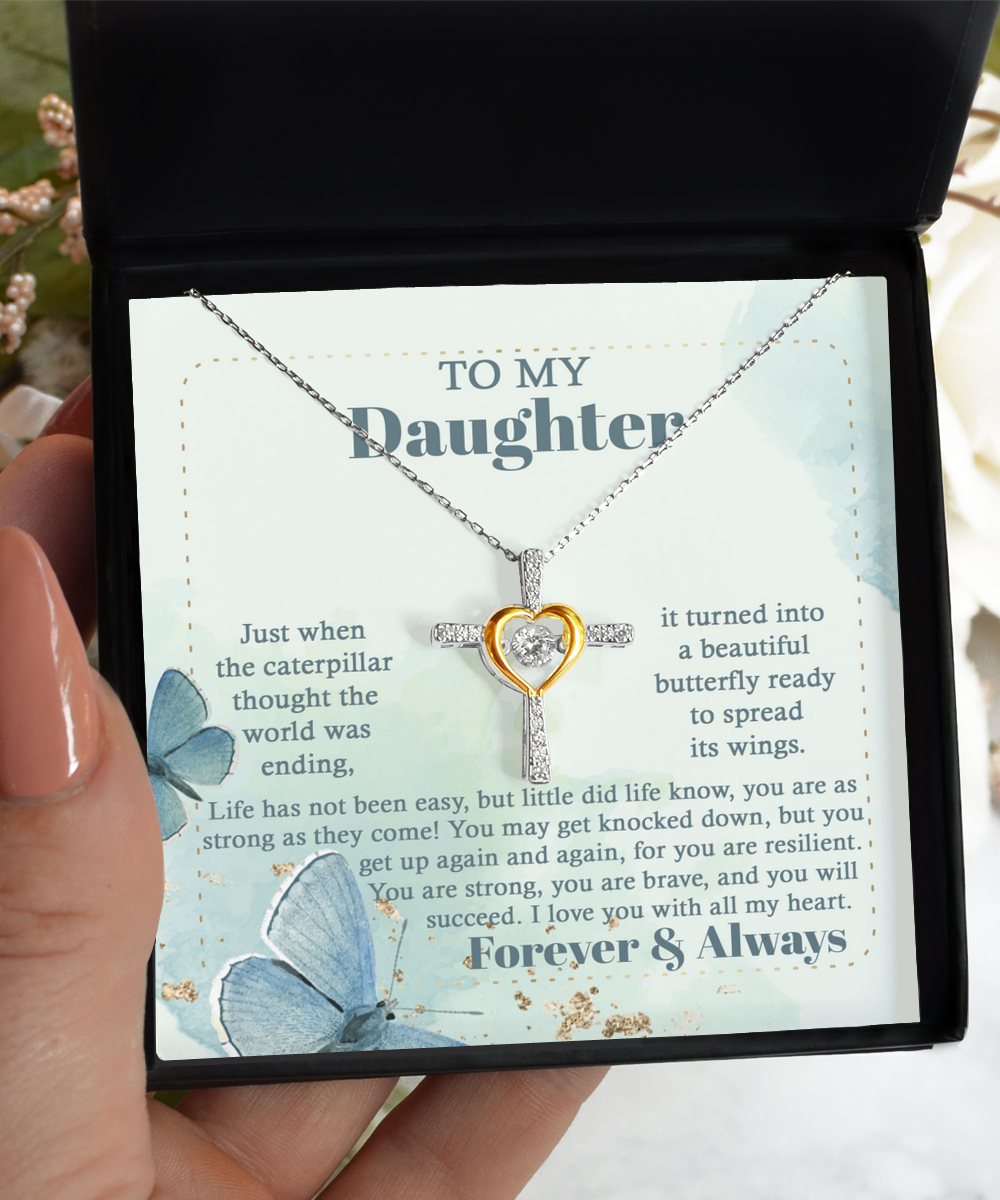 A hand holding an open jewelry box displays a beautiful "To Daughter-Beautiful Butterfly - Cross Dancing Necklace" in sterling silver, adorned with a heart and cross design featuring a central diamond. The box features a heartfelt message to a daughter, set against the backdrop of butterflies and flowers.