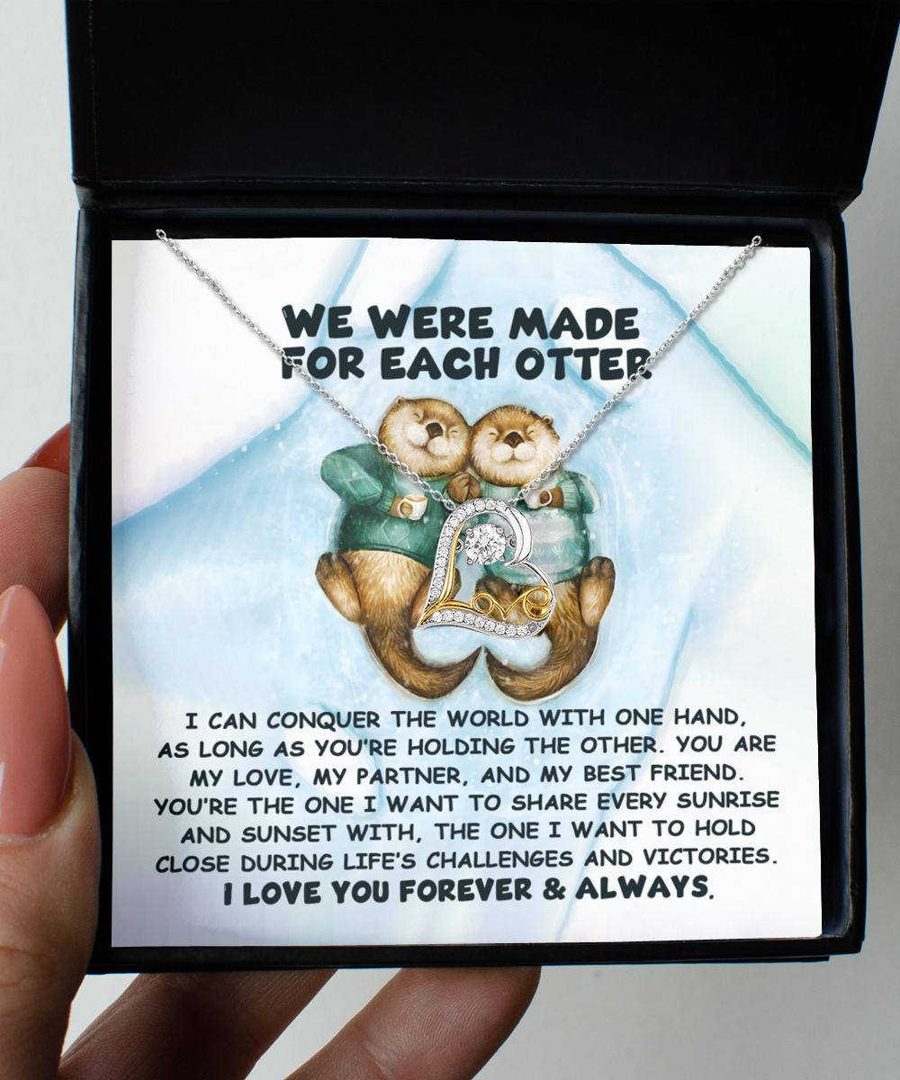 A person holds an open box revealing the "Soulmate- For Each Otter - Love Dancing Necklace," a Sterling Silver piece adorned with two otters and a heart pendant, complete with a romantic message.