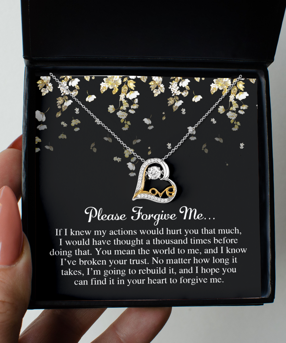 A hand holds an open box containing a 14k gold heart-shaped Sorry-Broken Your Trust - Love Dancing Necklace. The box lid reads, "Please Forgive Me," followed by an apology message.