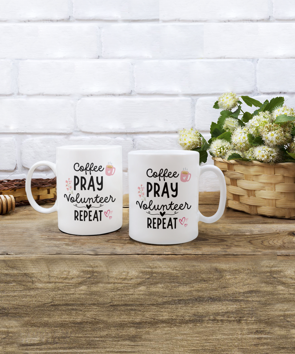 Two white "Coffee Pray Volunteer Repeat" mugs on a wooden table beside a wicker basket with white flowers, set against a brick wall. Limited time only, proudly printed and shipped from the USA.