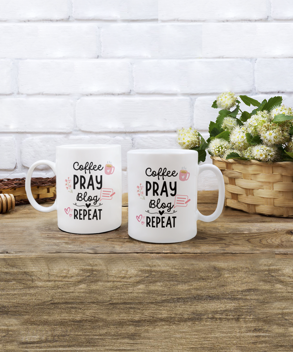 Two white "Coffee Pray Blog Repeat" mugs rest on wood, with flowers in the backdrop. These special edition Coffee Pray Blog Repeat Coffee Mugs are printed and shipped from the USA, ensuring a secure checkout for your peace of mind.