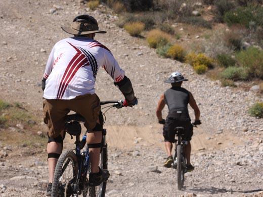 Two guys riding off-road downhill on mountain bikes wearing Da Brim Sporty Cycling.