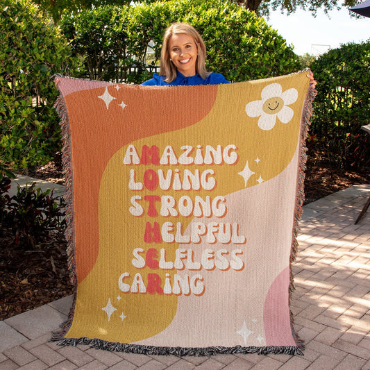 A mother holding up a Golden Value SG blanket that says Amazing Loving Mother Definition Heirloom Woven Blanket.