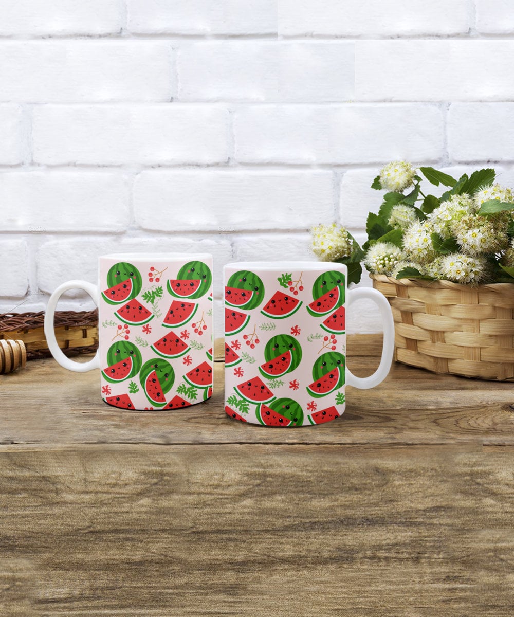 Two matching Cute Watermelon Print Mugs on Pink Background by Gearbubble on a wooden table against a white brick background, next to a basket with white flowers.