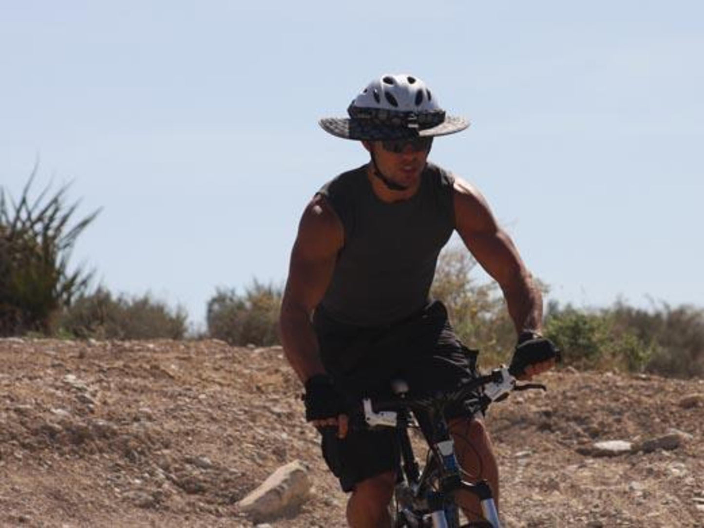 A young man riding off-road on a mountain bike wearing Da Brim Sporty Cycling.