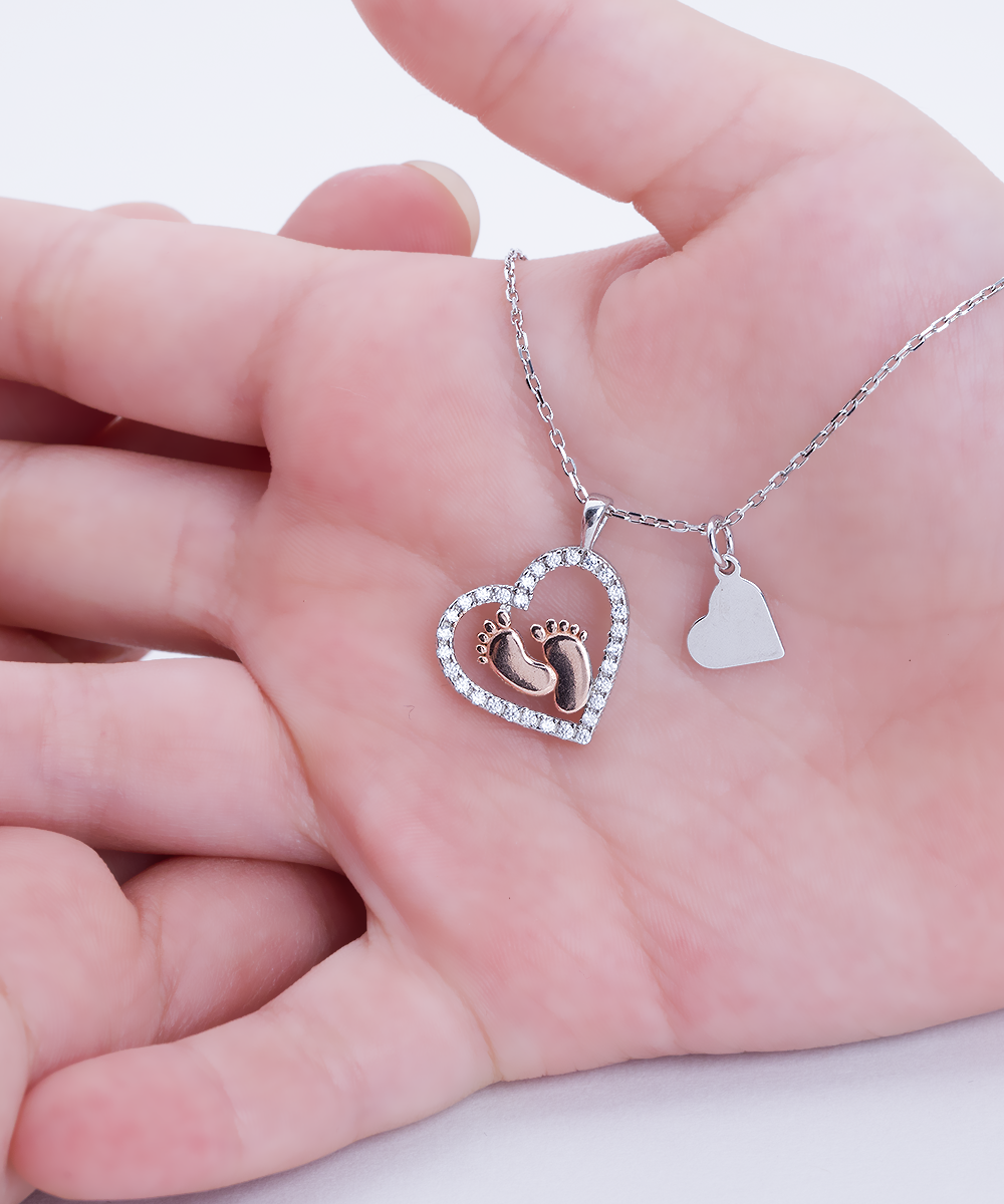 A hand holding a heart-shaped Gearbubble To My Mommy, Great Stories - Baby feet necklace with a baby's feet imprint on it.